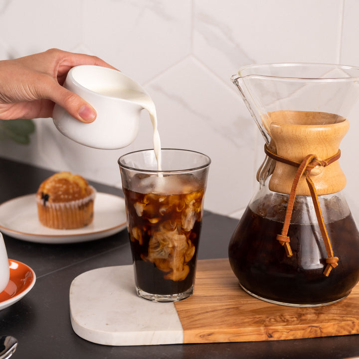 A woman pours a freshly brewed Chemex pour over into a Compass Coffee mug at home.