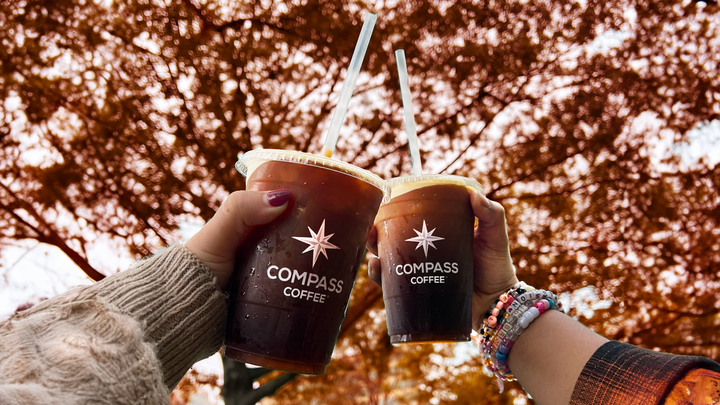 Two cups of cold brew held up to a tree showing autumn leaves.